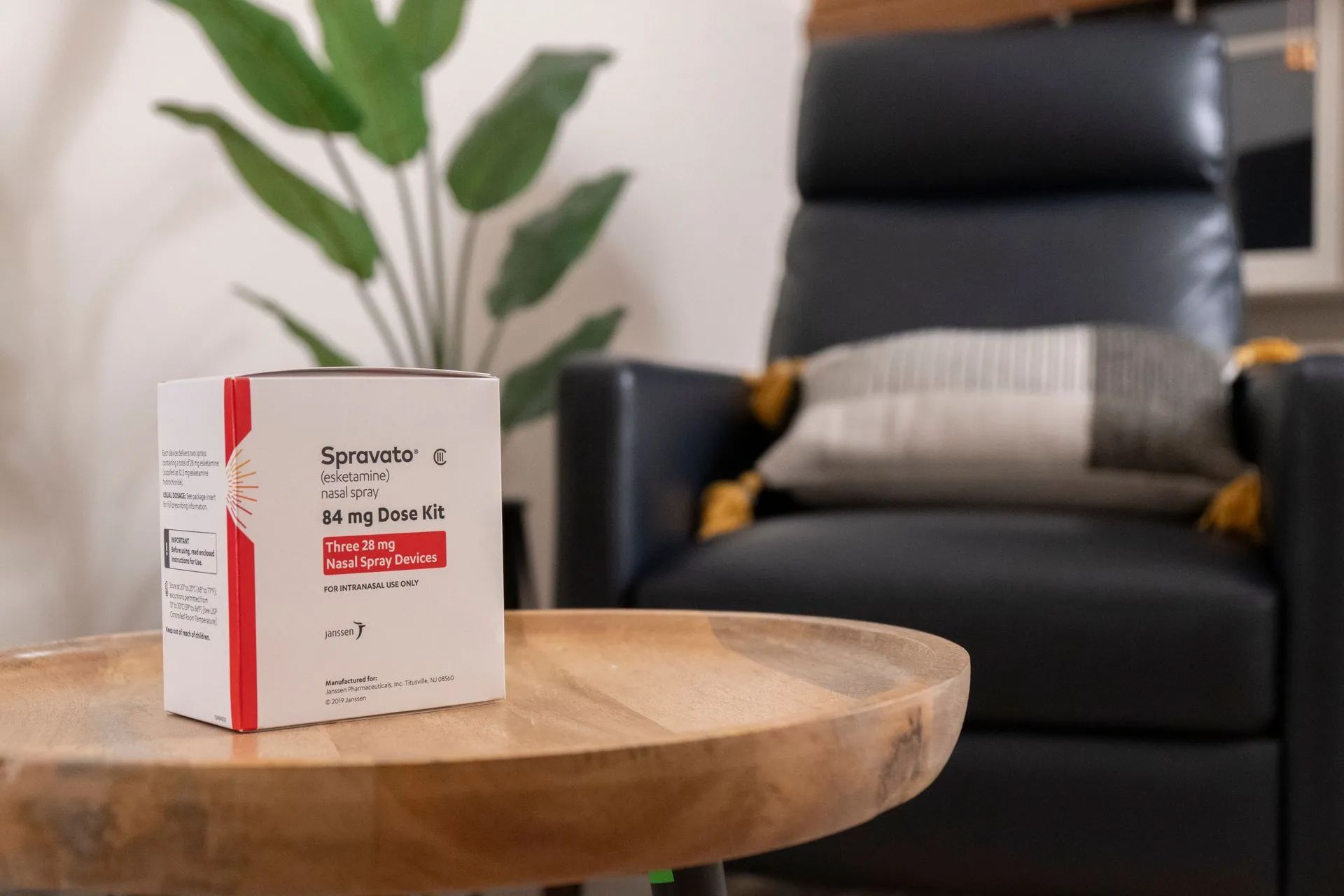 Box of Spironolactone pills on a wooden table, with a recliner and plant in the background.