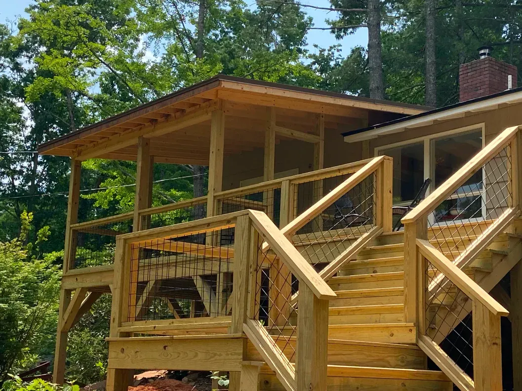 Wooden deck and porch with stairs, surrounded by trees.
