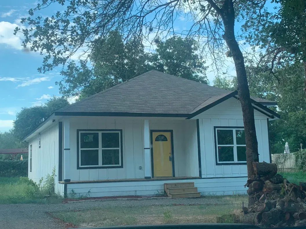 Small white house under construction with a yellow door; brown roof.