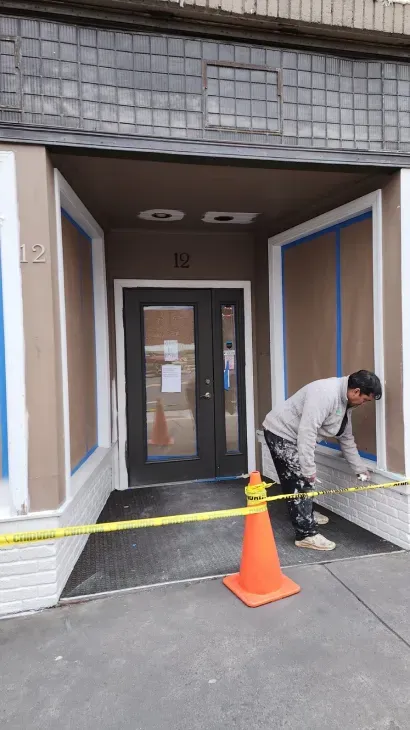 Man painting building entrance with tape and caution tape visible.