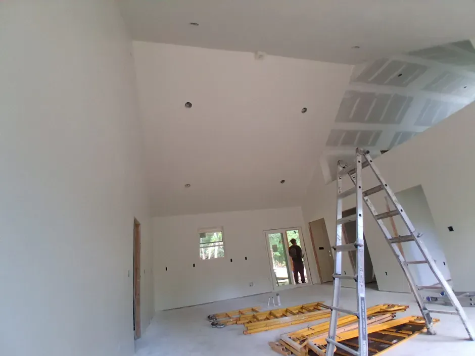 Interior of a room under construction with a high ceiling, drywall, and a ladder.
