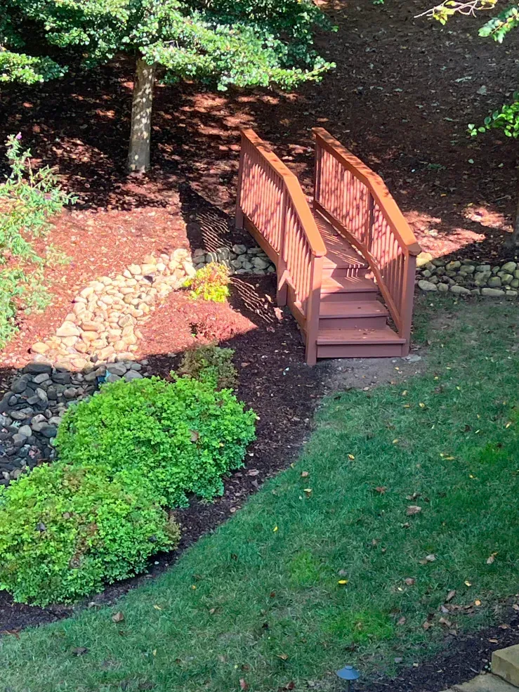 Wooden bridge over a landscaped area with grass and shrubs.