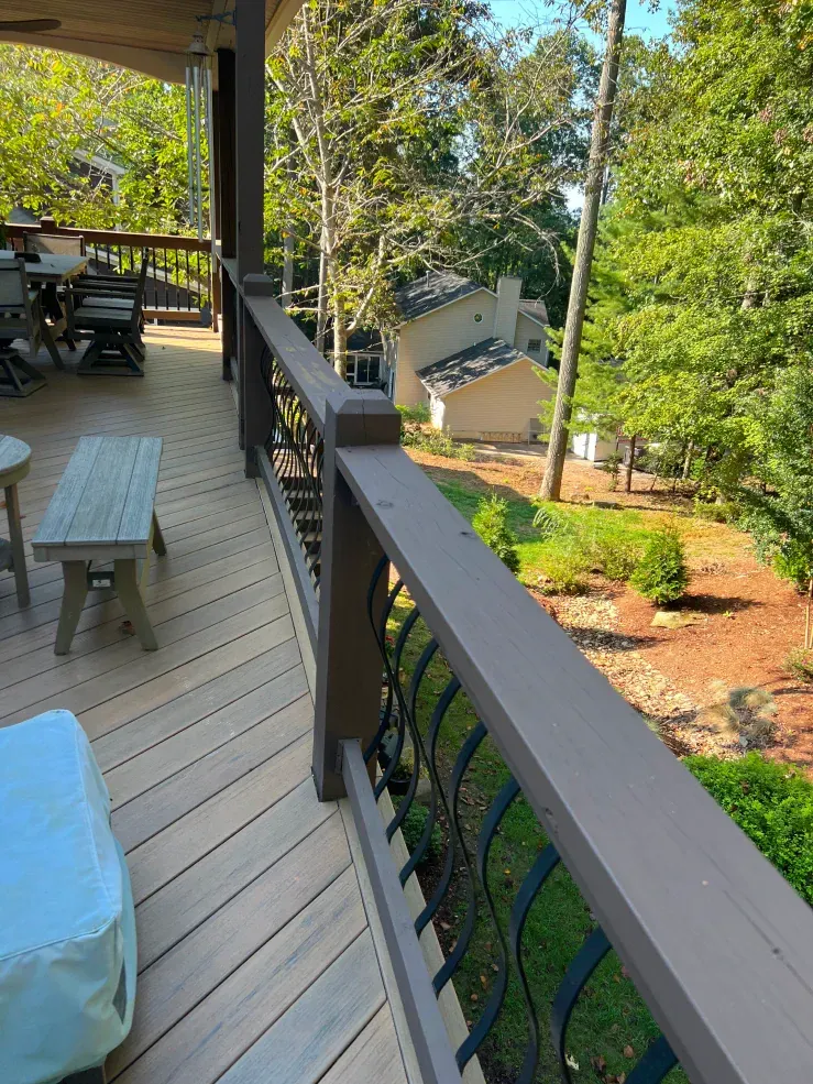 Deck with brown railings overlooking a yard with trees and a building.
