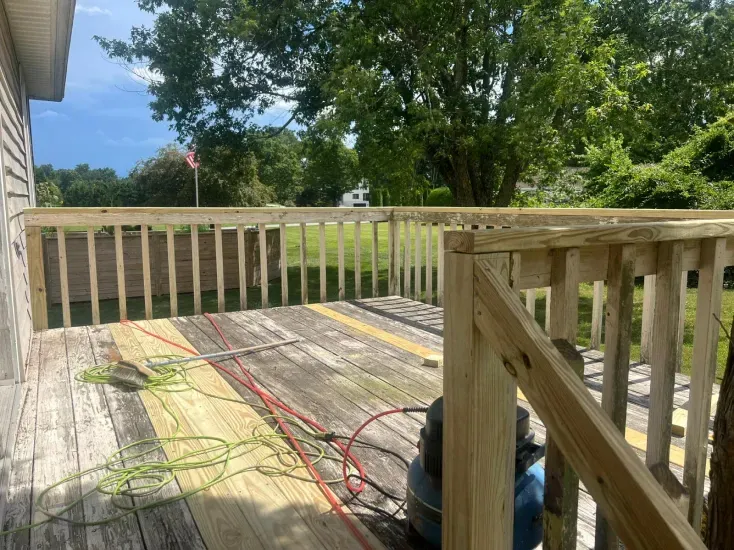 Wooden deck with new railing being built. Old, weathered deck with some tools visible.
