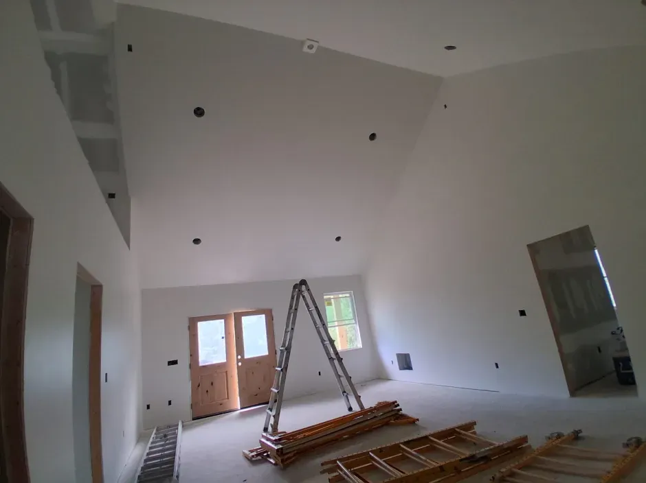 Interior of a room under construction with white walls, unfinished doors and windows, and a ladder.