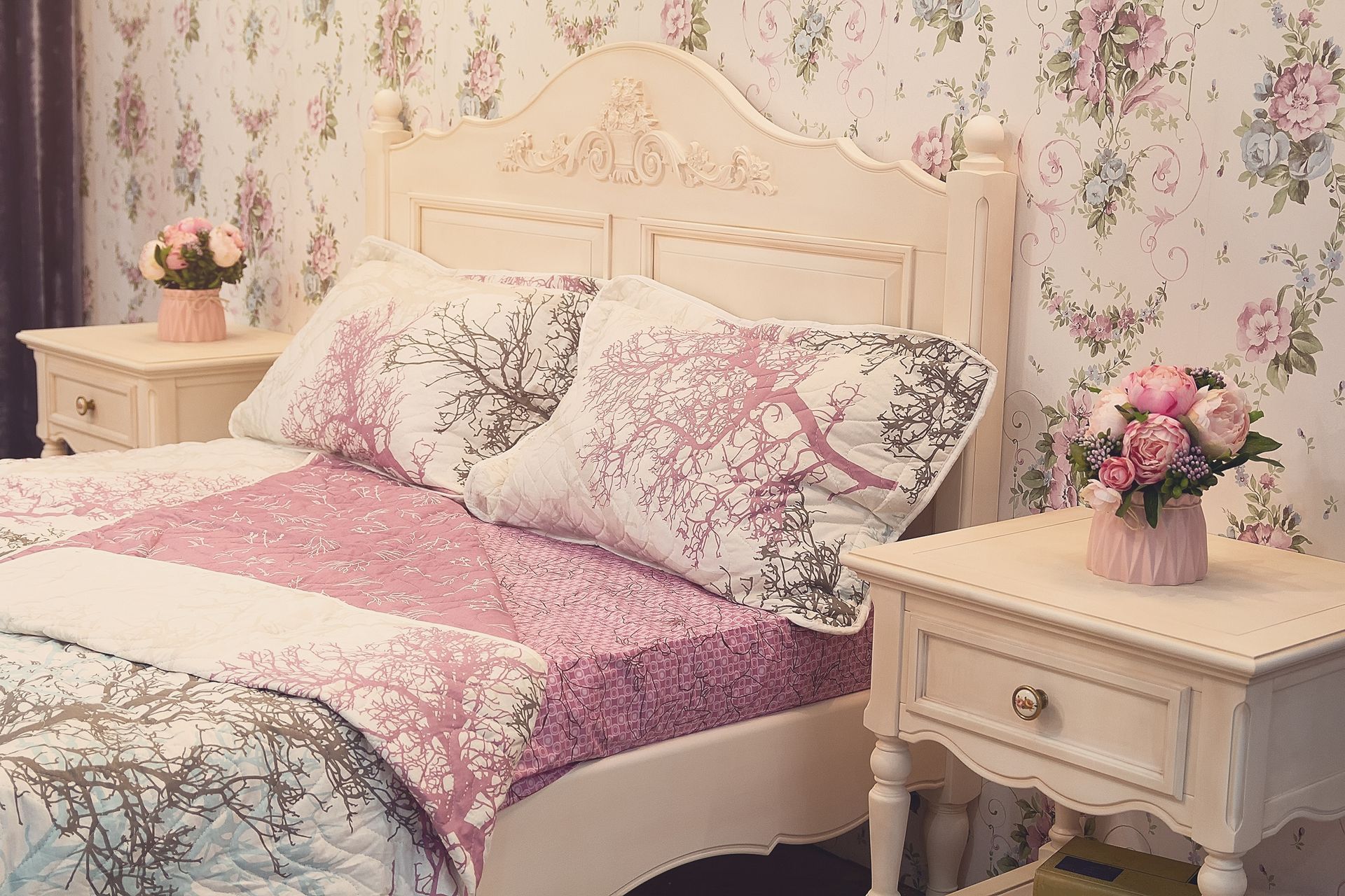 Bedroom with floral wallpaper and a bed with pink and white bedding. Two nightstands with flowers.