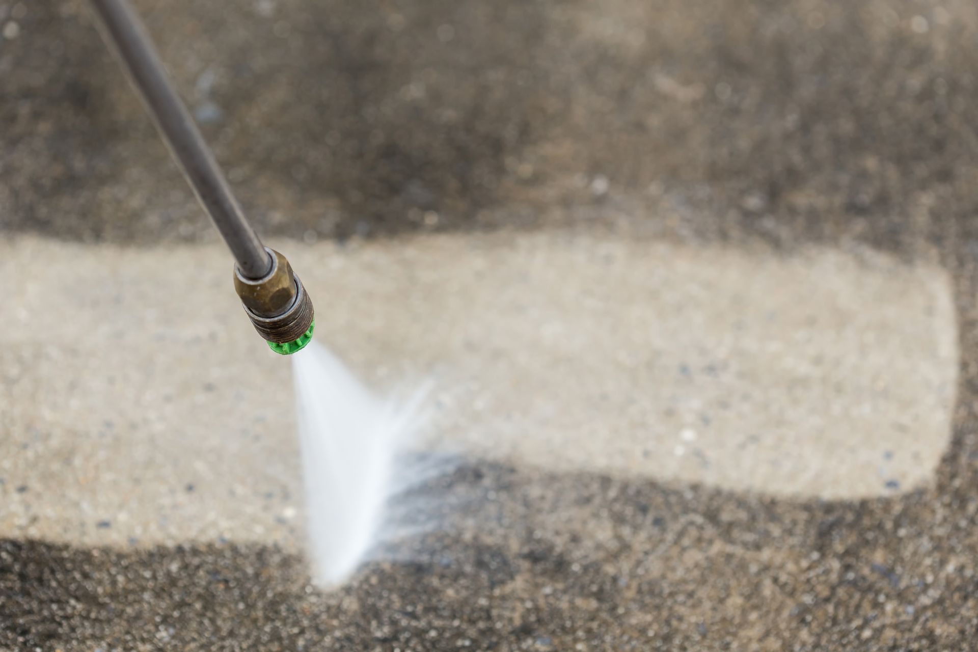 Power washer spraying a concrete surface, cleaning a white strip.