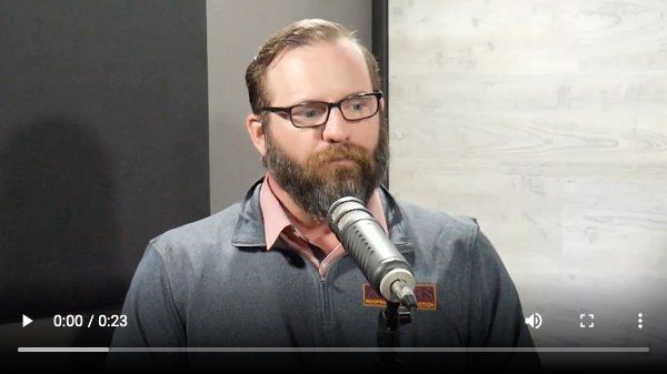A man with a beard and glasses is speaking into a microphone.