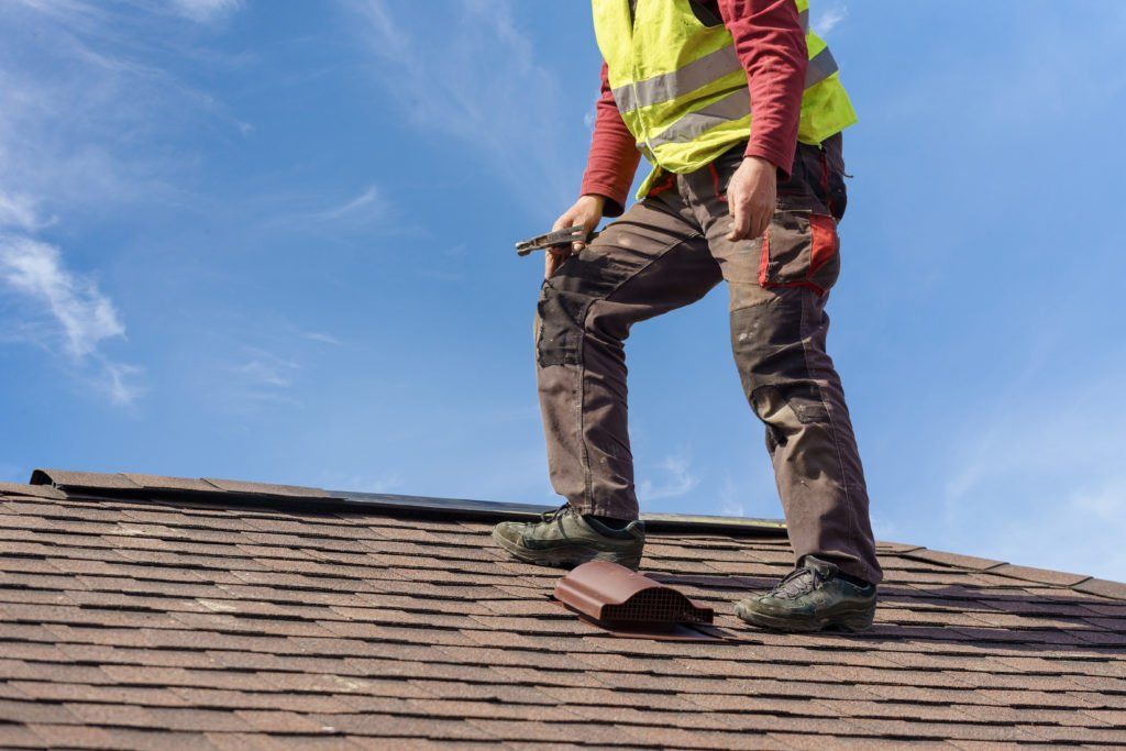 A man is standing on top of a roof holding a hammer.