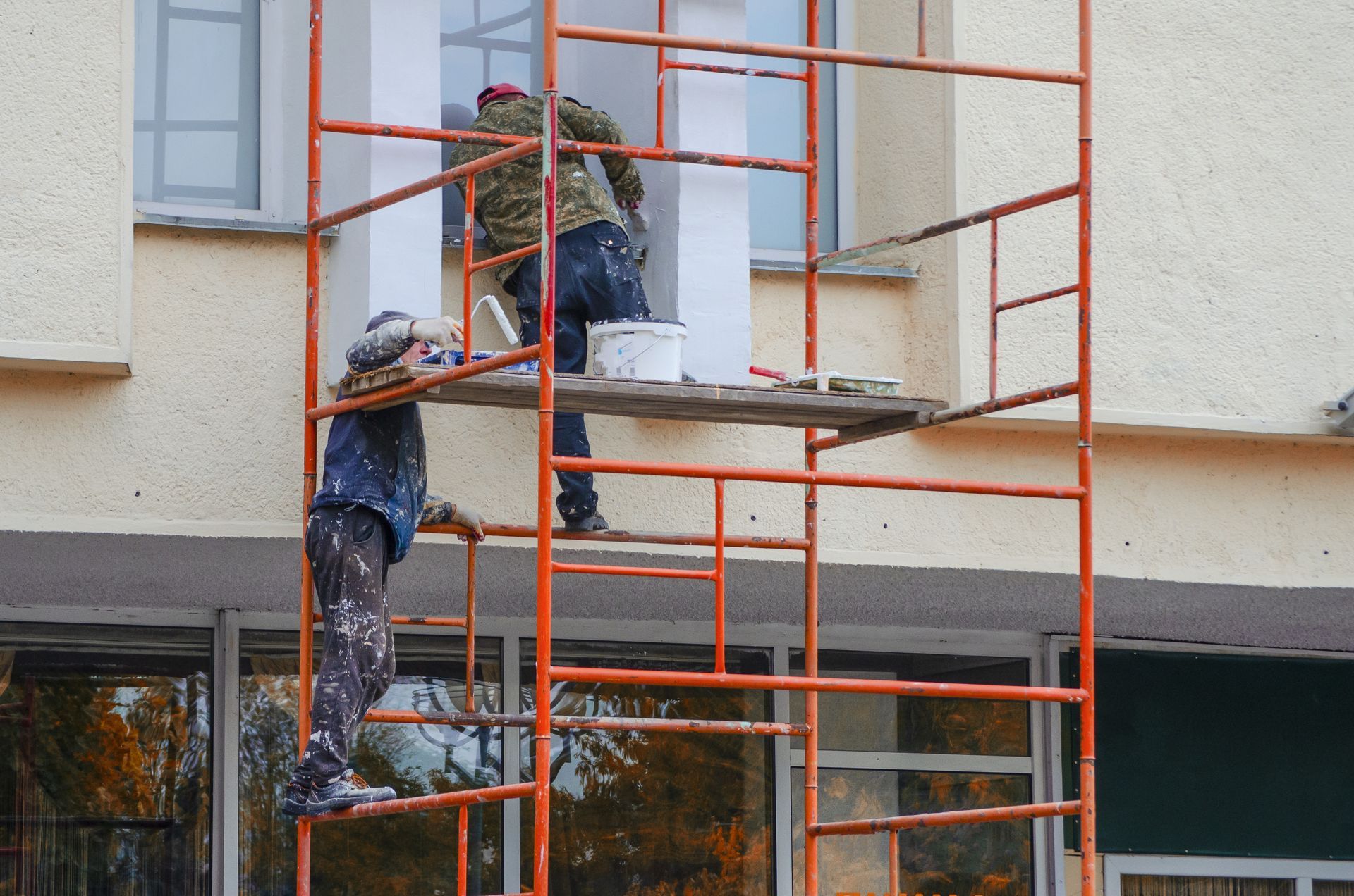 Two professional painters diligently working together, applying fresh coats of paint to the exterior of a building.
