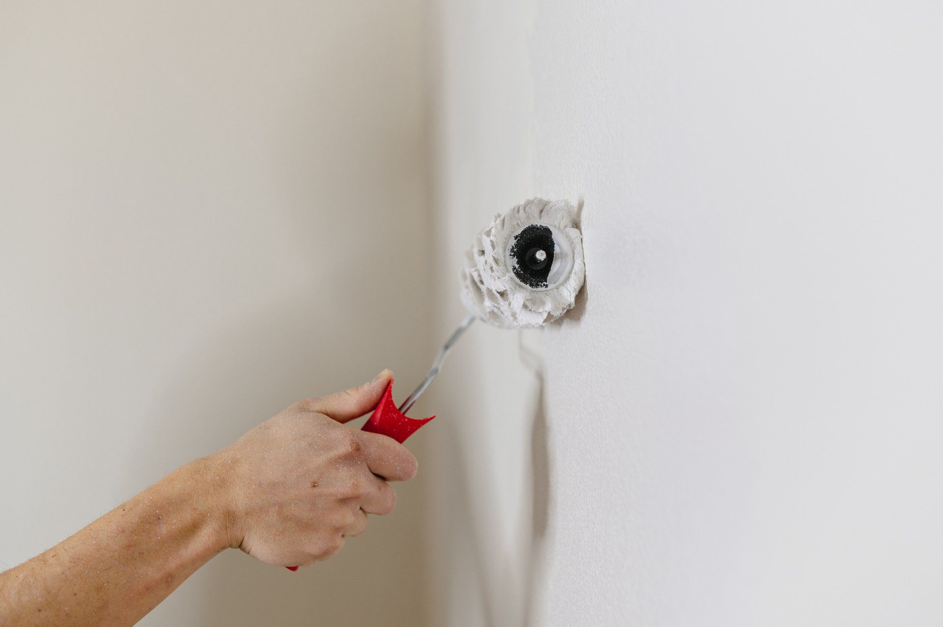 A close-up view of a hand holding a paint roller and applying paint to an interior wall.