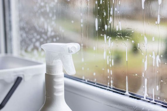 A spray bottle is sitting on a window sill next to a bucket.