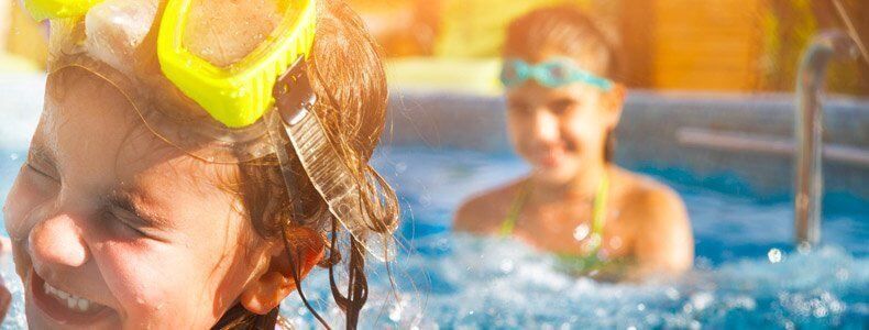 Two children wearing swimming goggles smile while playing in a sunny pool. Two children wearing swimming goggles smile while playing in a sunny pool.