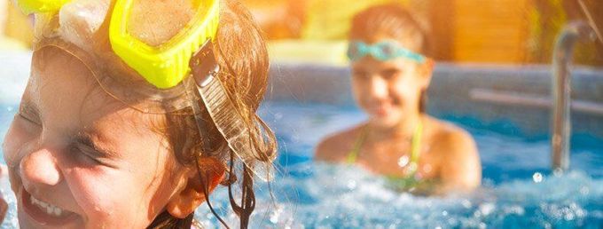 Two children wearing swimming goggles smile while playing in a sunny pool. Two children wearing swimming goggles smile while playing in a sunny pool.