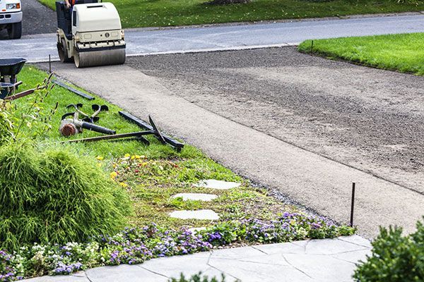 a man is using a roller to spread asphalt on a driveway .