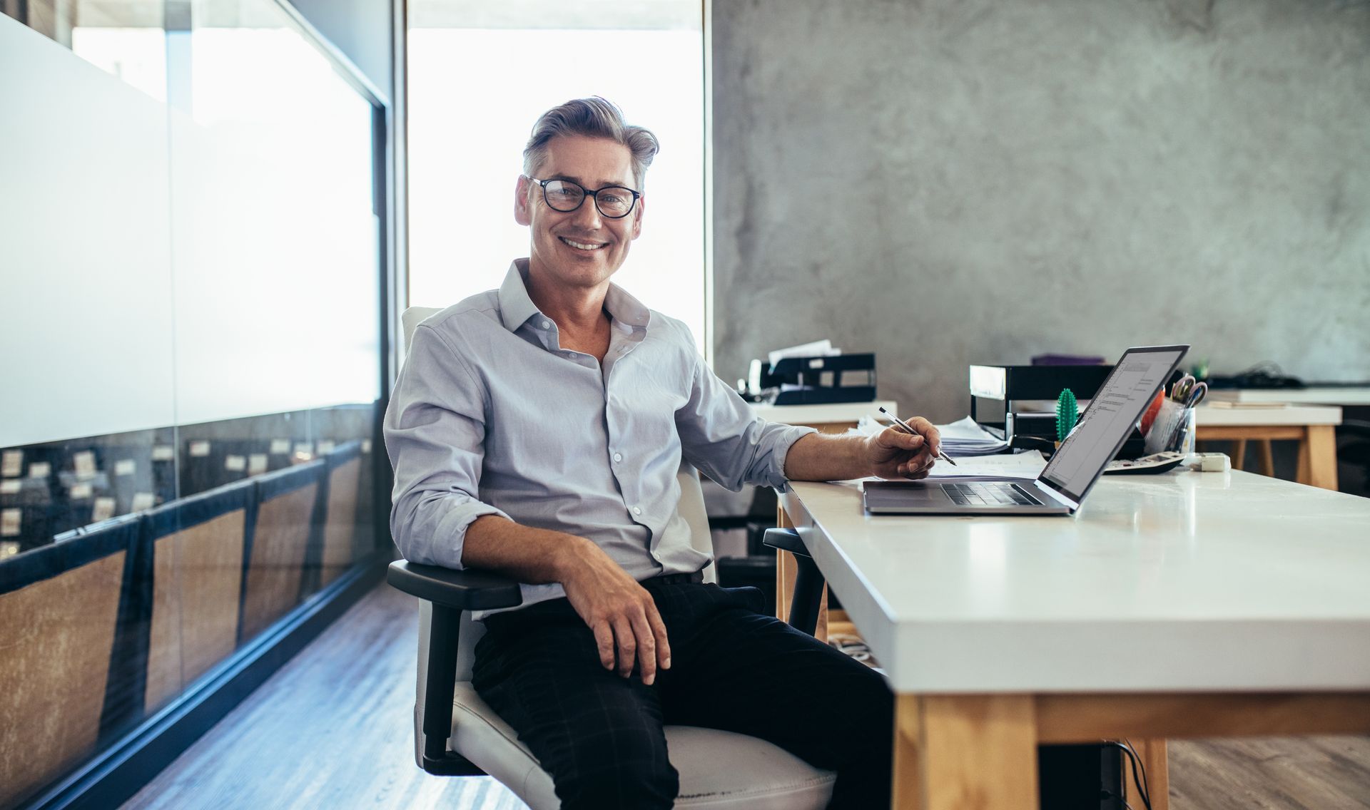 Person smiling at a desk with a laptop in a modern office space Person smiling at a desk with a laptop in a modern office space