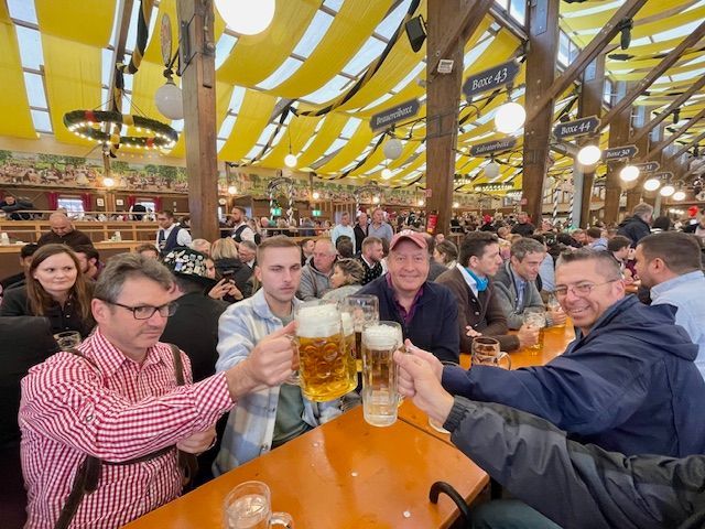 Two mugs of beer, sausages, and sauerkraut on a wooden table at an outdoor gathering.