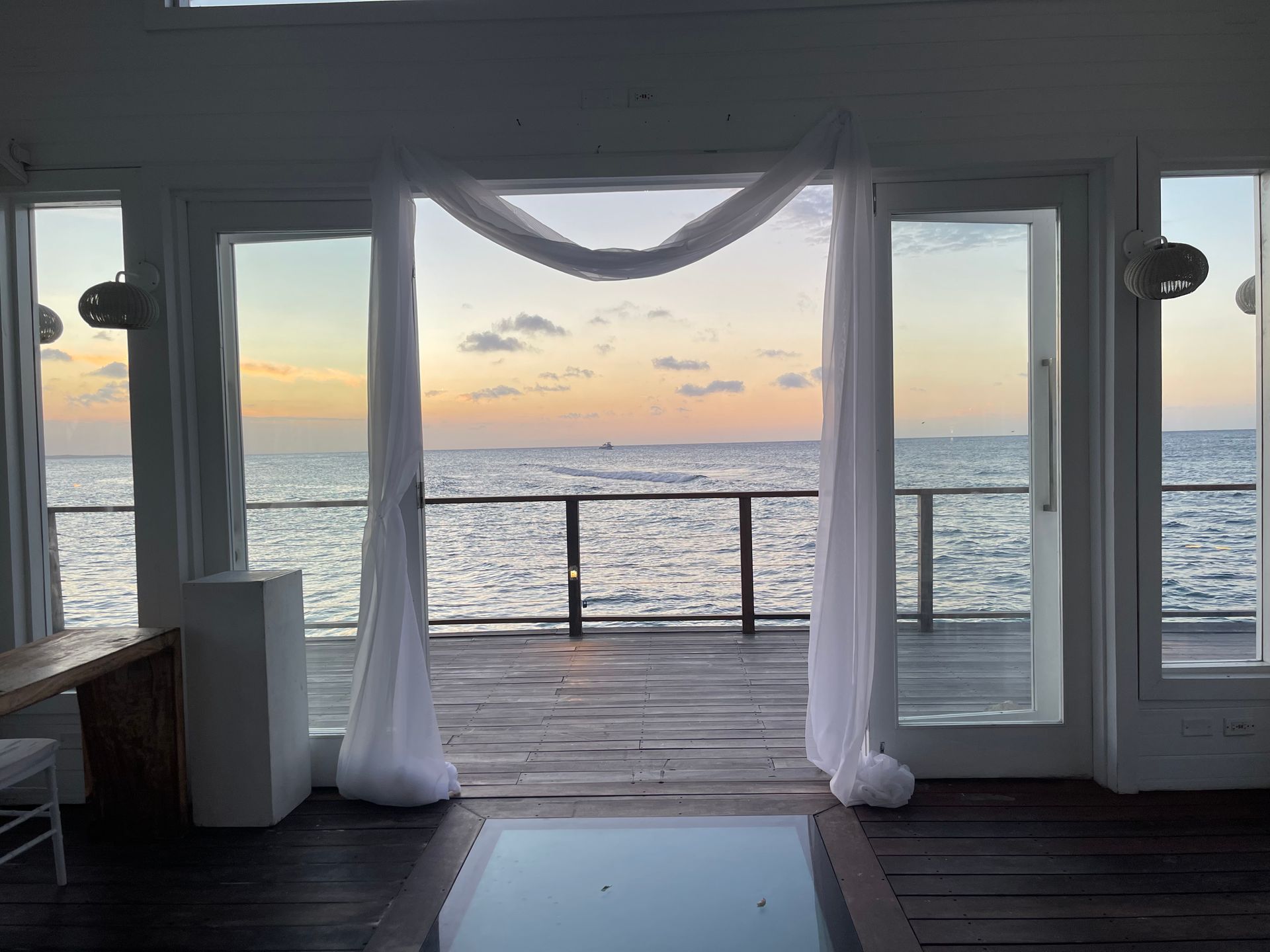 Interior view with draped doorway overlooking ocean at sunset.
