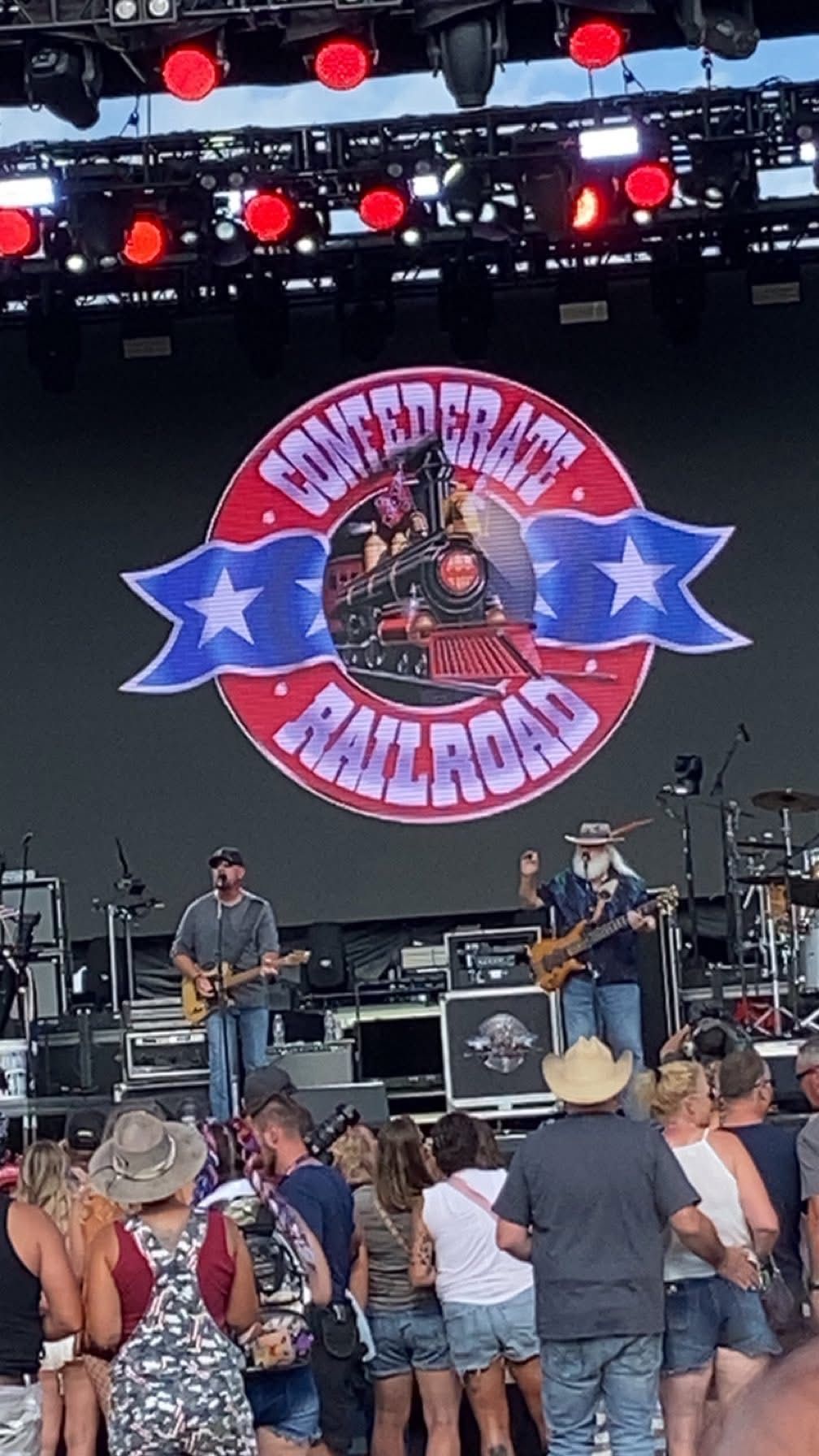 Confederate Railroad band on stage, performing in front of a crowd. Large logo on screen.