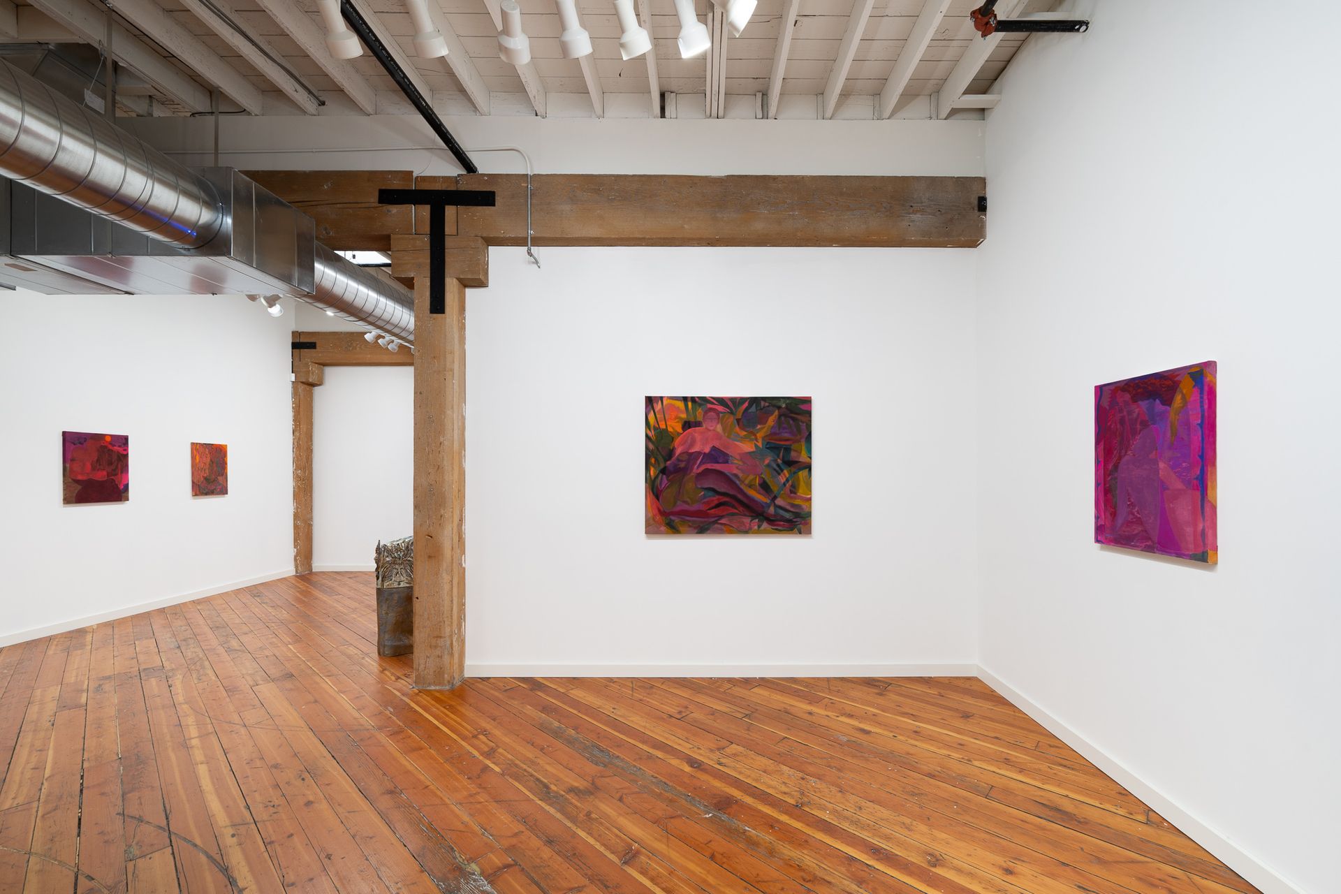 An art gallery with white walls and hardwood floors displaying four colorful abstract paintings by Emily Elizabeth Wise.