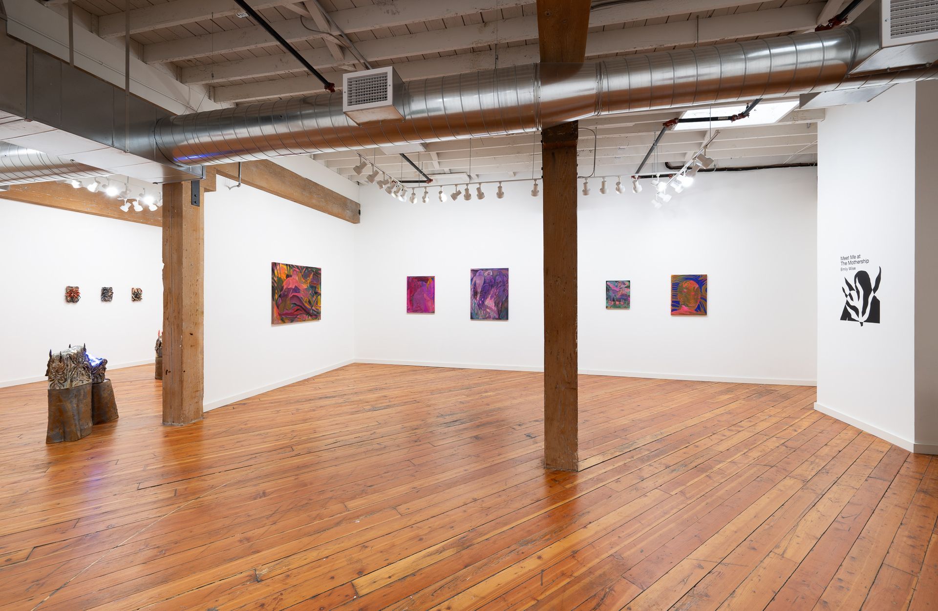 An art gallery space with wooden floors, white walls hung with colorful paintings by Emily Elizabeth Wise.