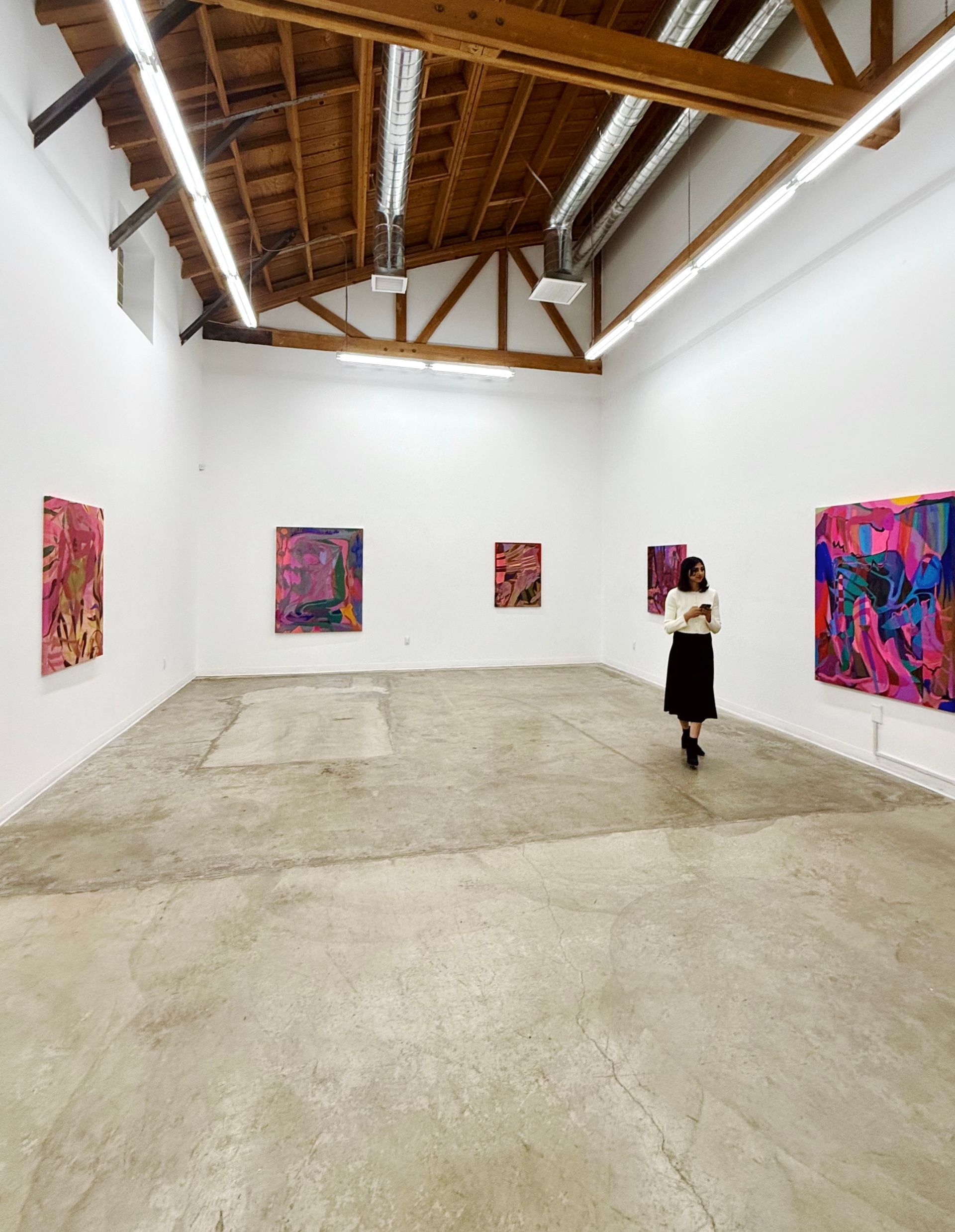 Art gallery with five colorful abstract paintings on white walls; a person walks through space.