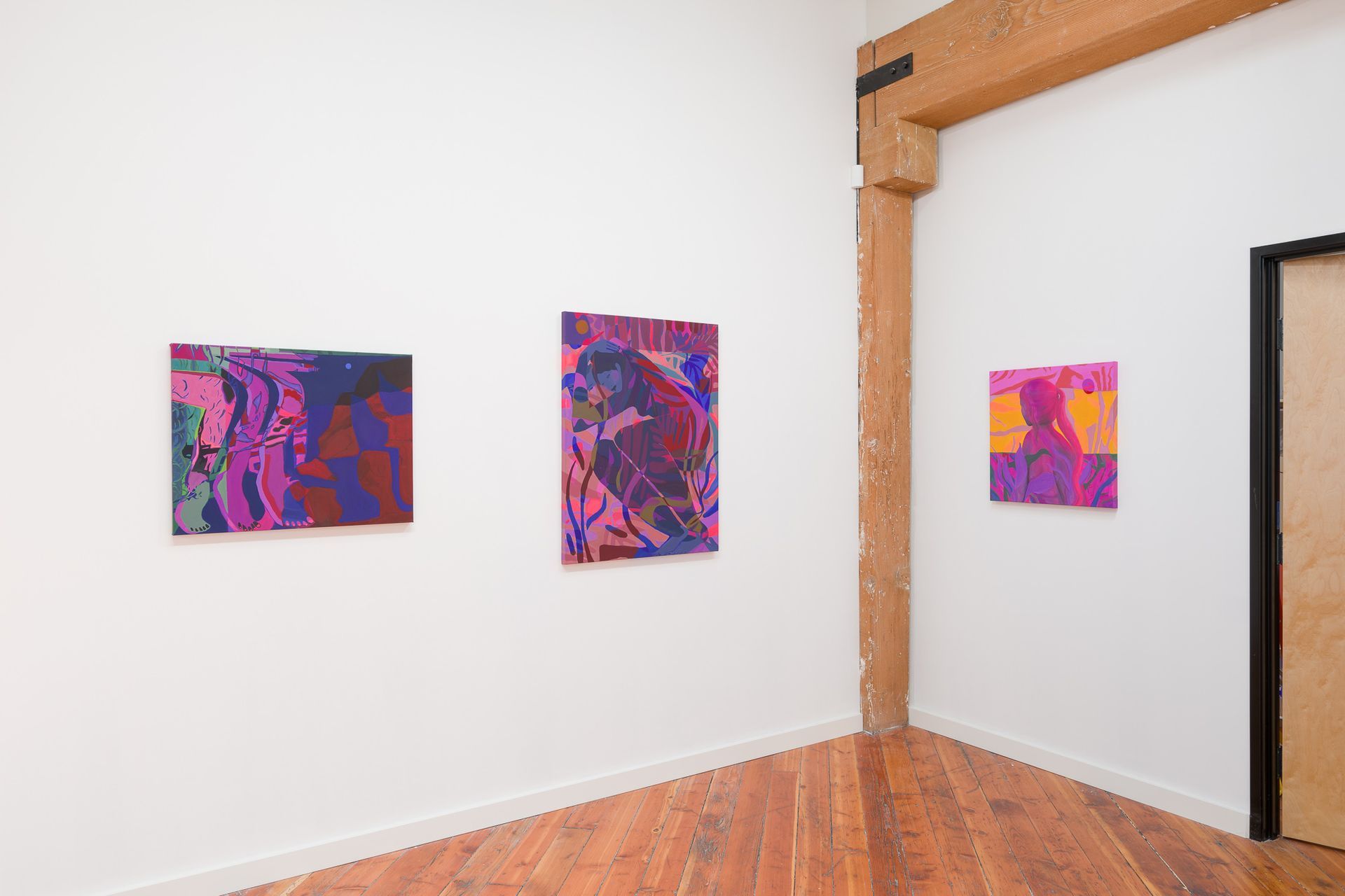 Three colorful abstract paintings by Emily Wise displayed in a gallery with wood floors and a structural beam.
