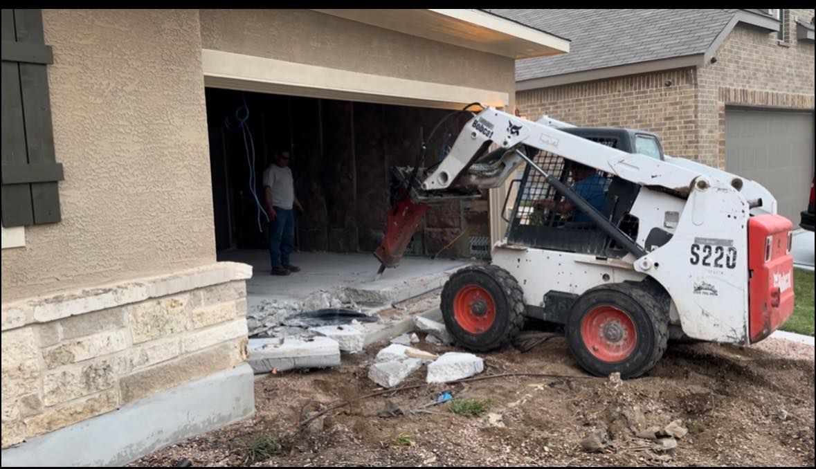 A Bobcat demolishes a garage, while a man watches. Exterior of a home.
