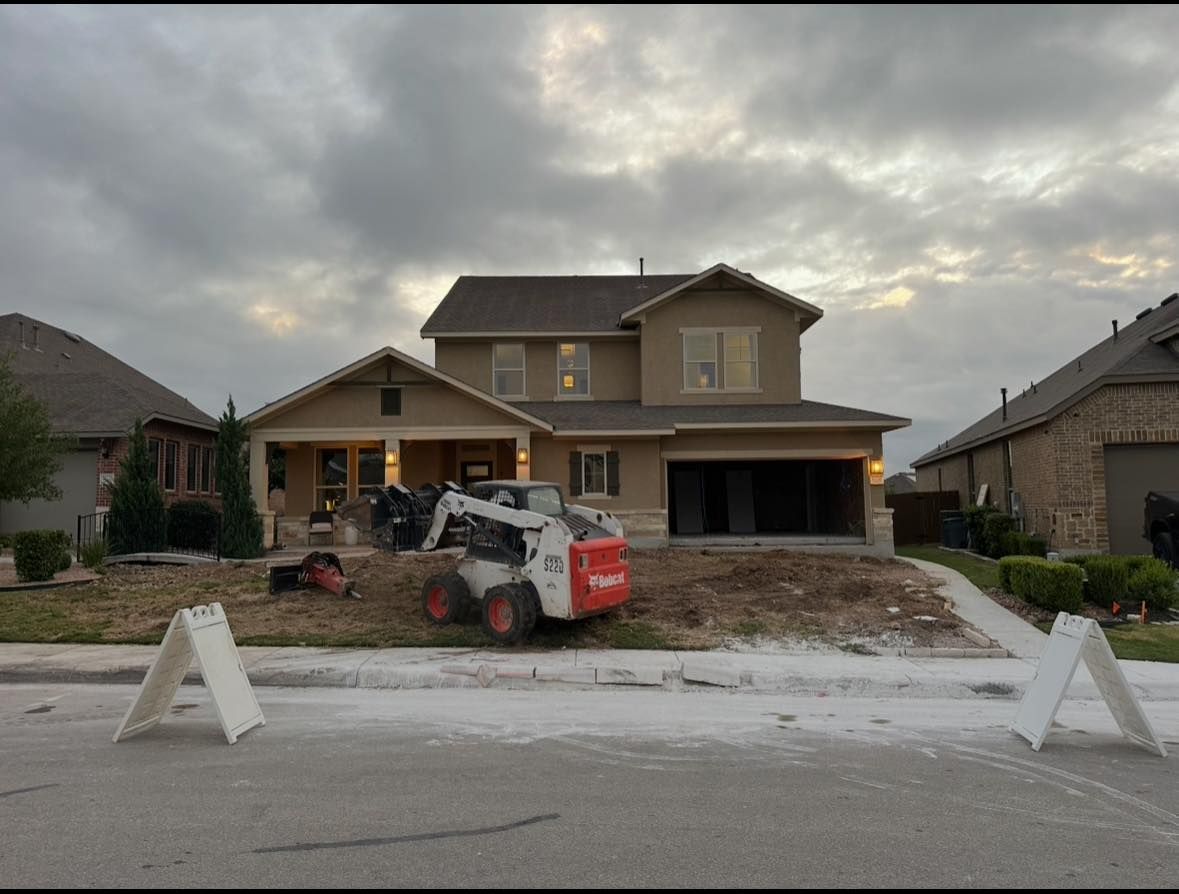 A two-story house with a bobcat in the yard during a landscaping project, under a cloudy sky.