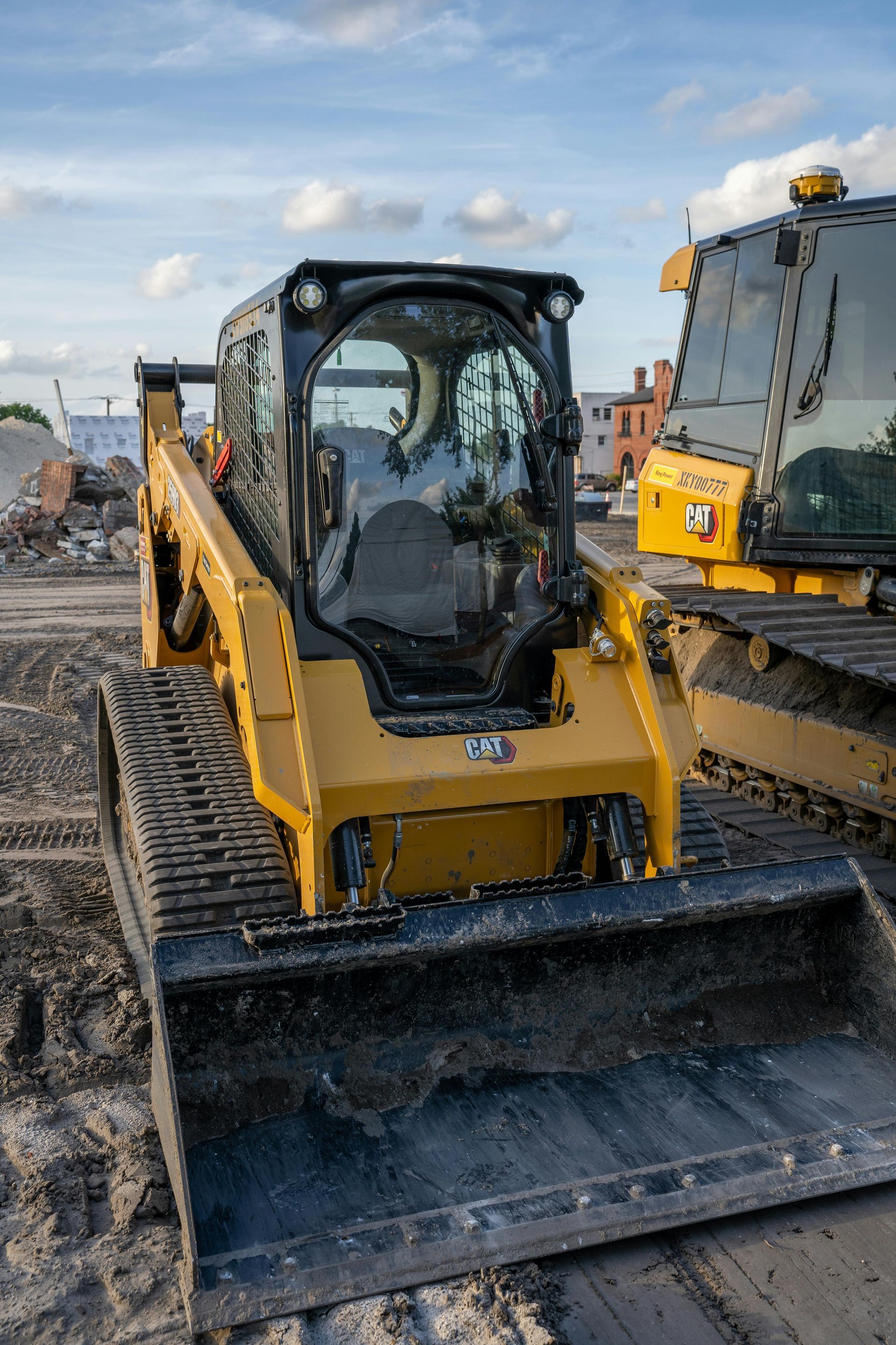 Yellow tracked skid steer with black cab and bucket on a construction site.