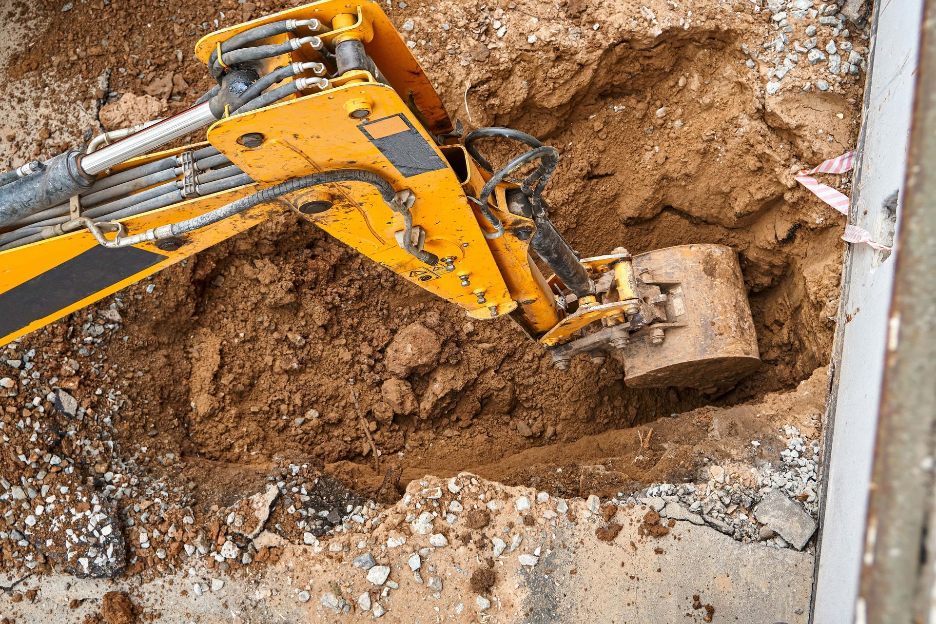 Yellow excavator digging a hole in brown earth near a concrete edge.