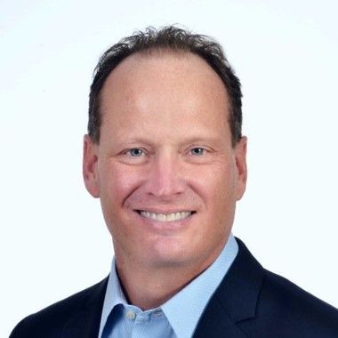 Portrait of a smiling man in a dark suit and light blue shirt against a white background