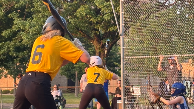 Softball players taking swings.