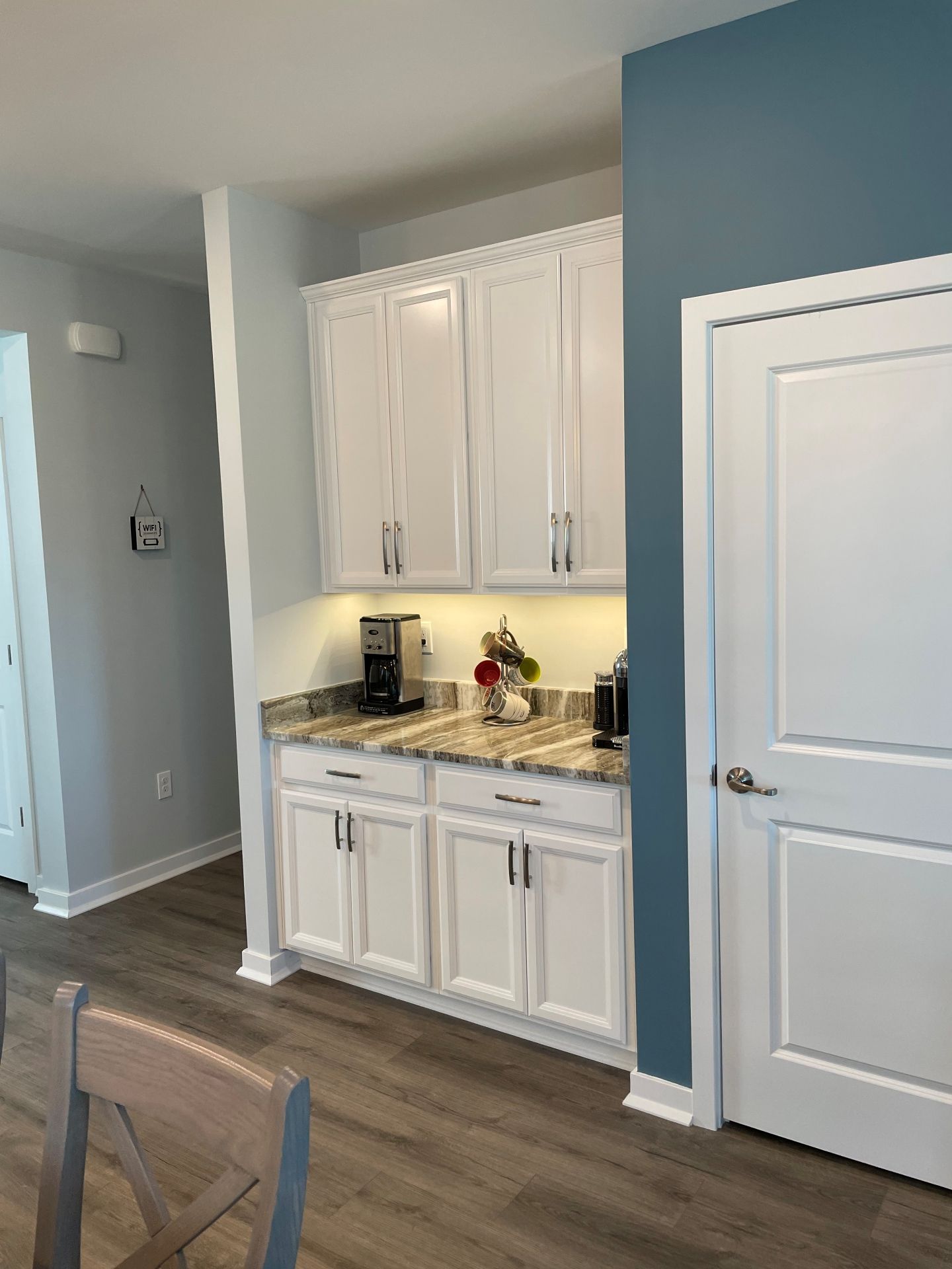 A white built-in cabinet and counter with a coffee maker, set against a dark blue accent wall in a home interior.