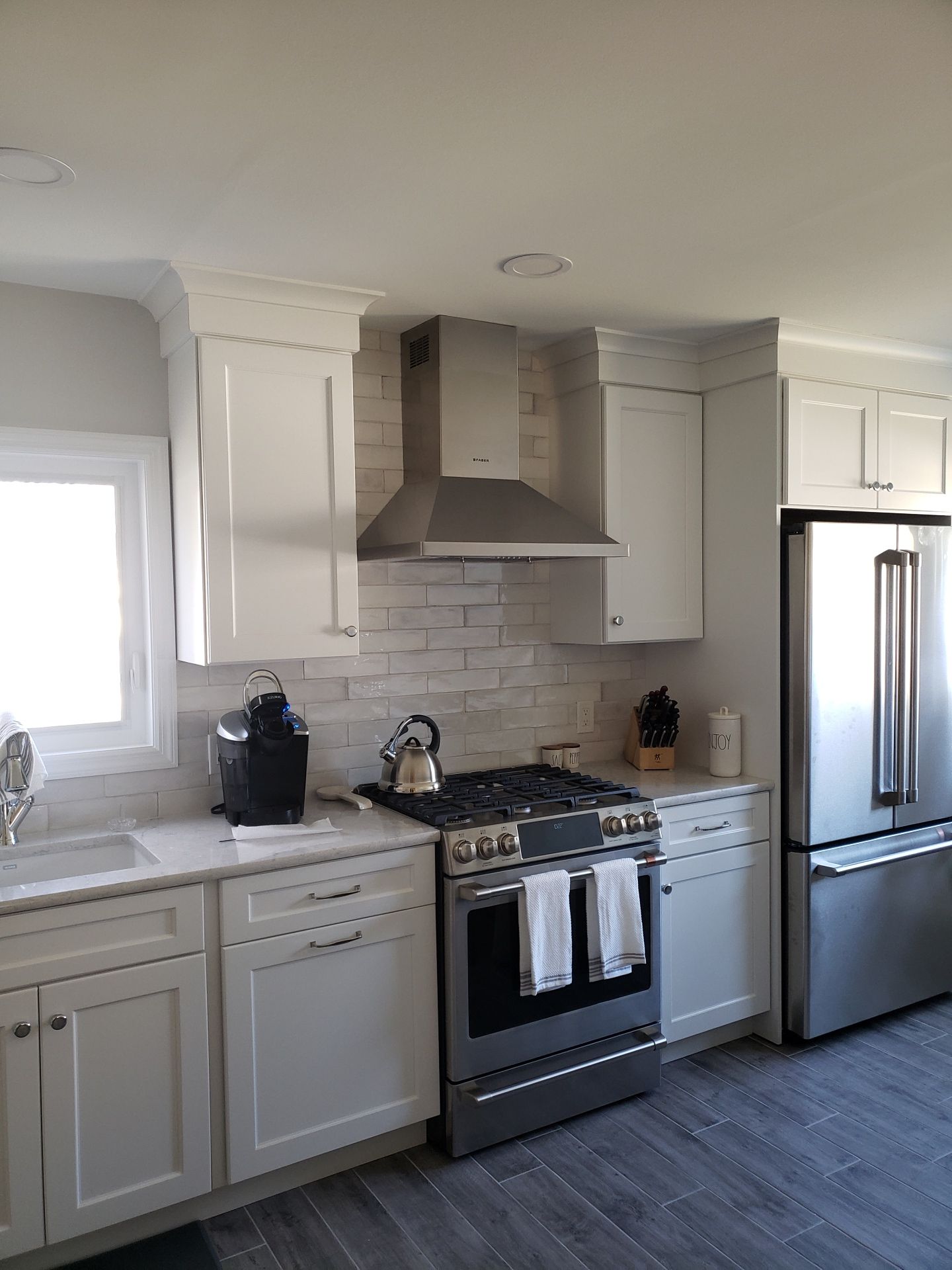 Modern kitchen with white cabinets, stainless steel appliances, a grey brick backsplash, and grey wood-look flooring.