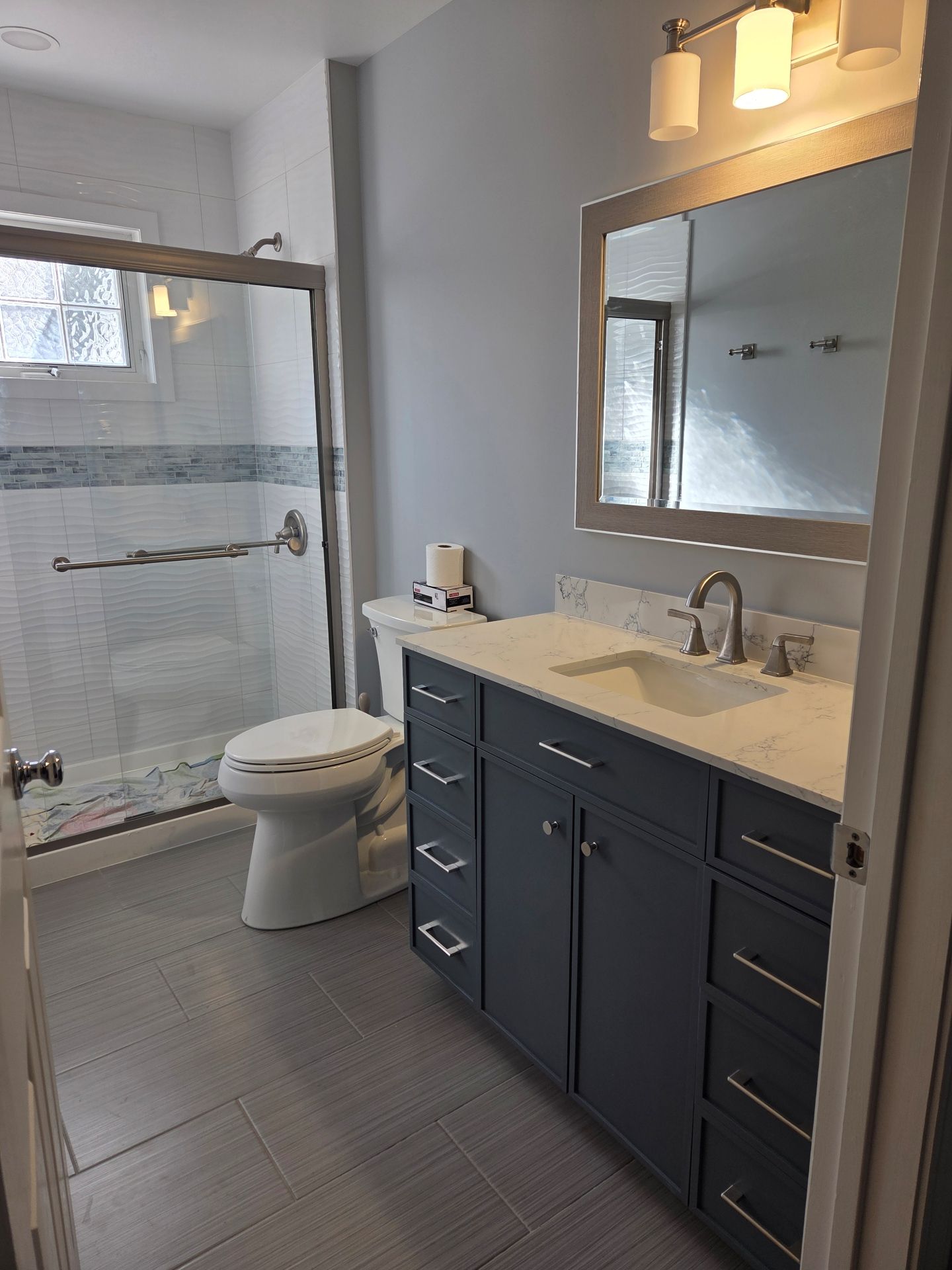 A modern bathroom featuring a gray vanity with a white countertop, a white toilet, and a glass-enclosed shower.
