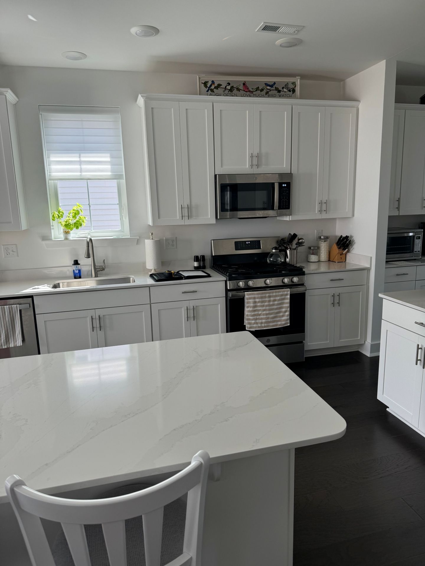 A modern white kitchen featuring a center island, white cabinetry, a gas stove, microwave, and dark hardwood floors.