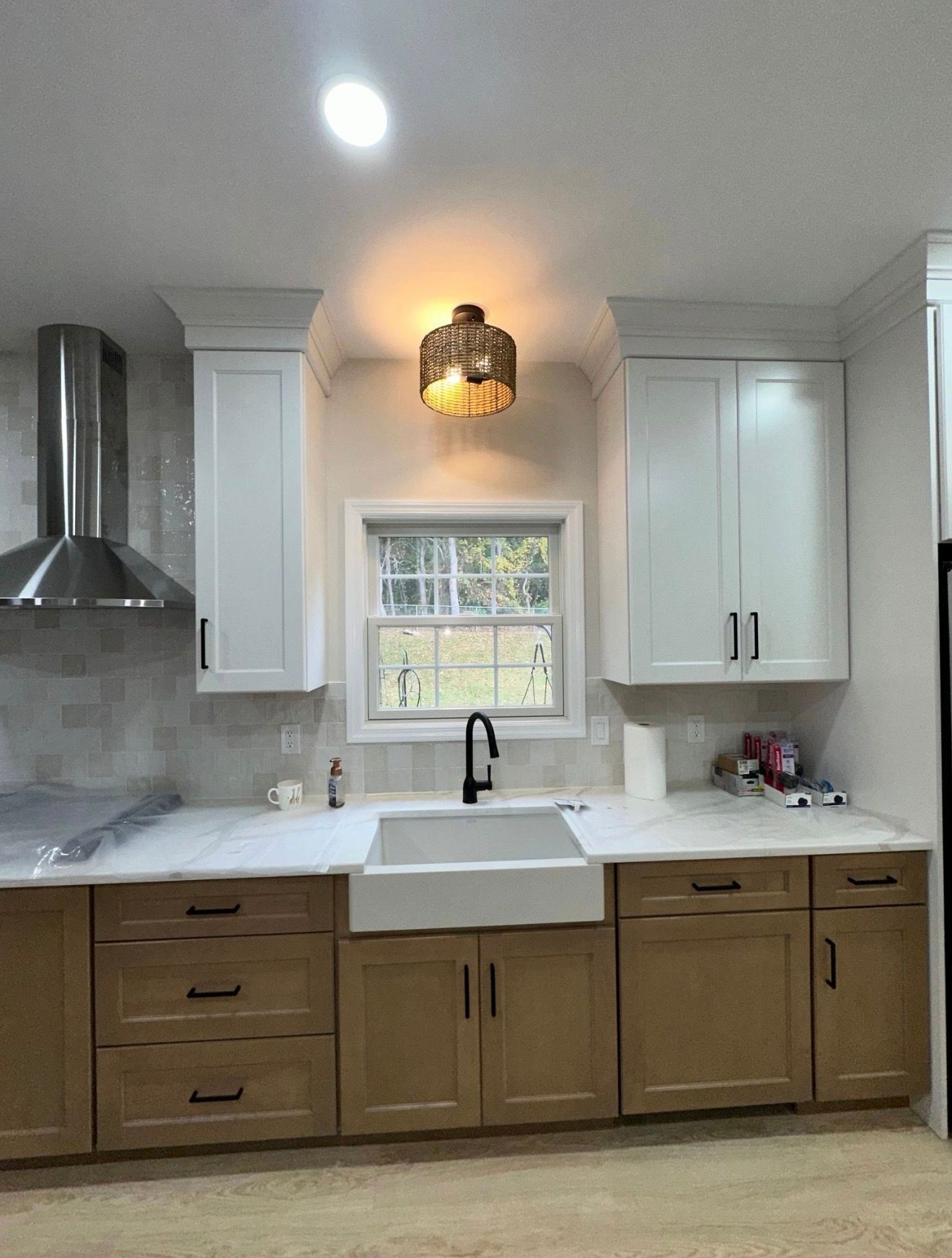 A kitchen featuring white upper cabinets, wood lower cabinets, a farmhouse sink, stainless steel hood, and a window.