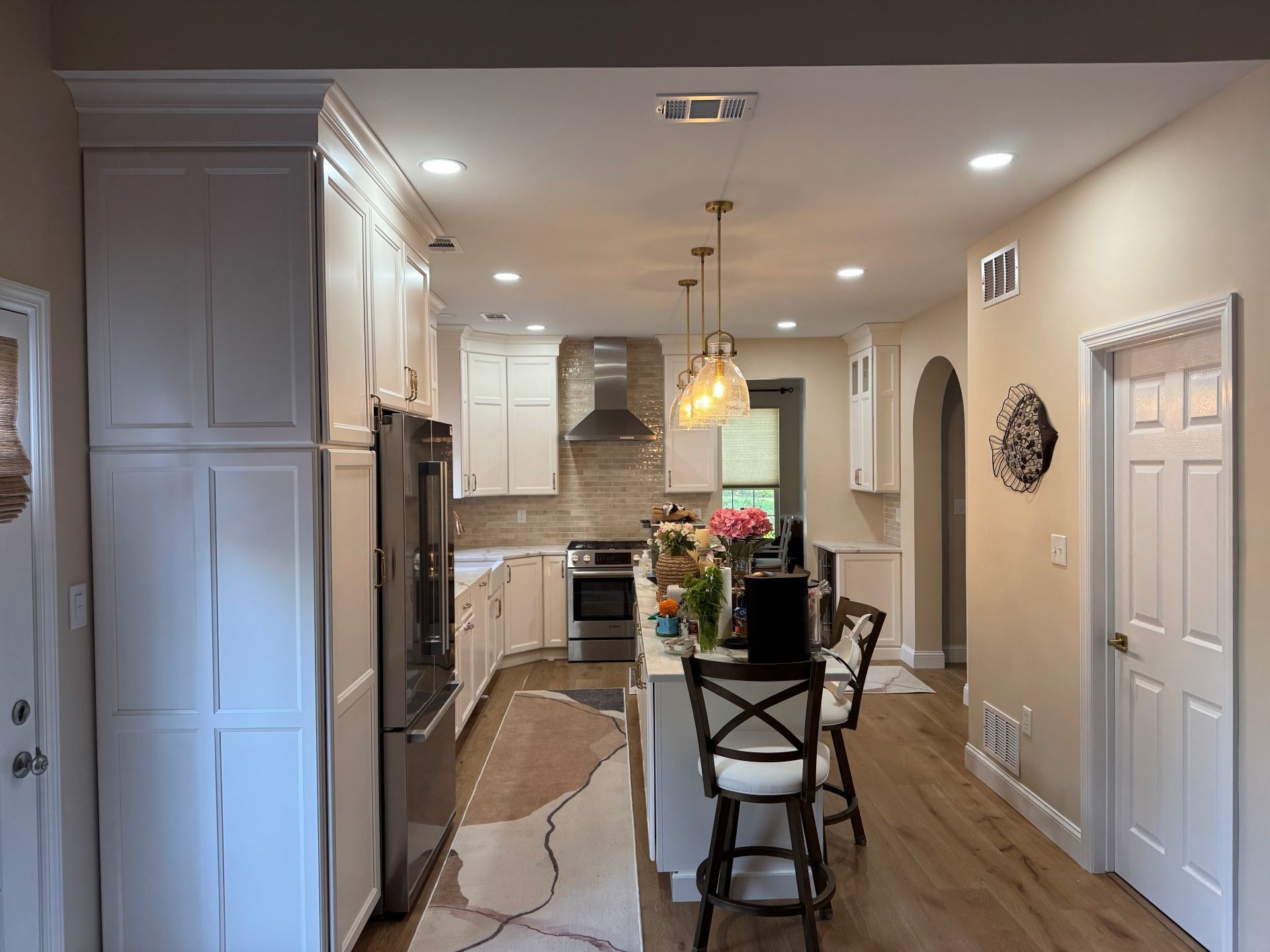 A bright kitchen featuring white cabinets, stainless steel appliances, a center island with bar stools, and wood flooring.