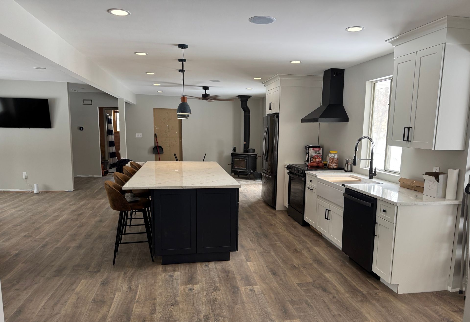 A modern kitchen with white cabinets, a dark island, stainless steel appliances, and wood-look flooring.