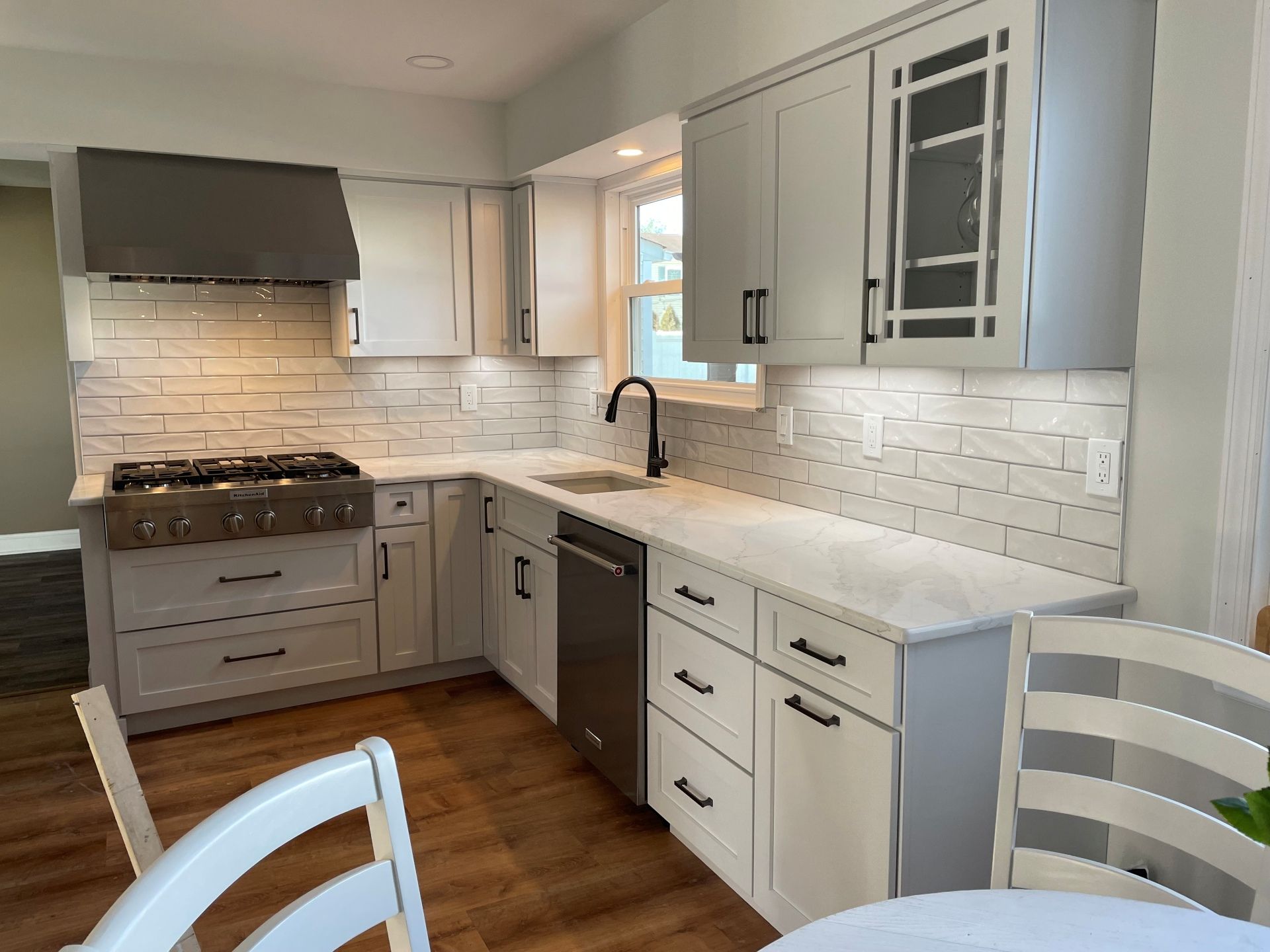 A modern kitchen with light gray cabinets, white subway tile backsplash, a stainless steel range, and wood-look flooring.