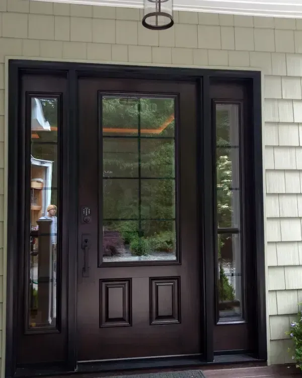 A dark-brown, six-paneled front door with a window divided into eight squares, framed by two vertical sidelight windows.