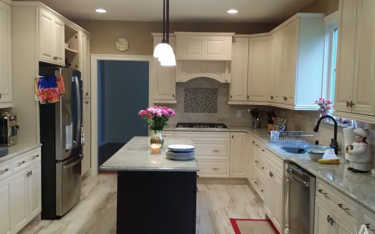 A modern kitchen with off-white cabinets, granite countertops, a dark kitchen island, and stainless steel appliances.