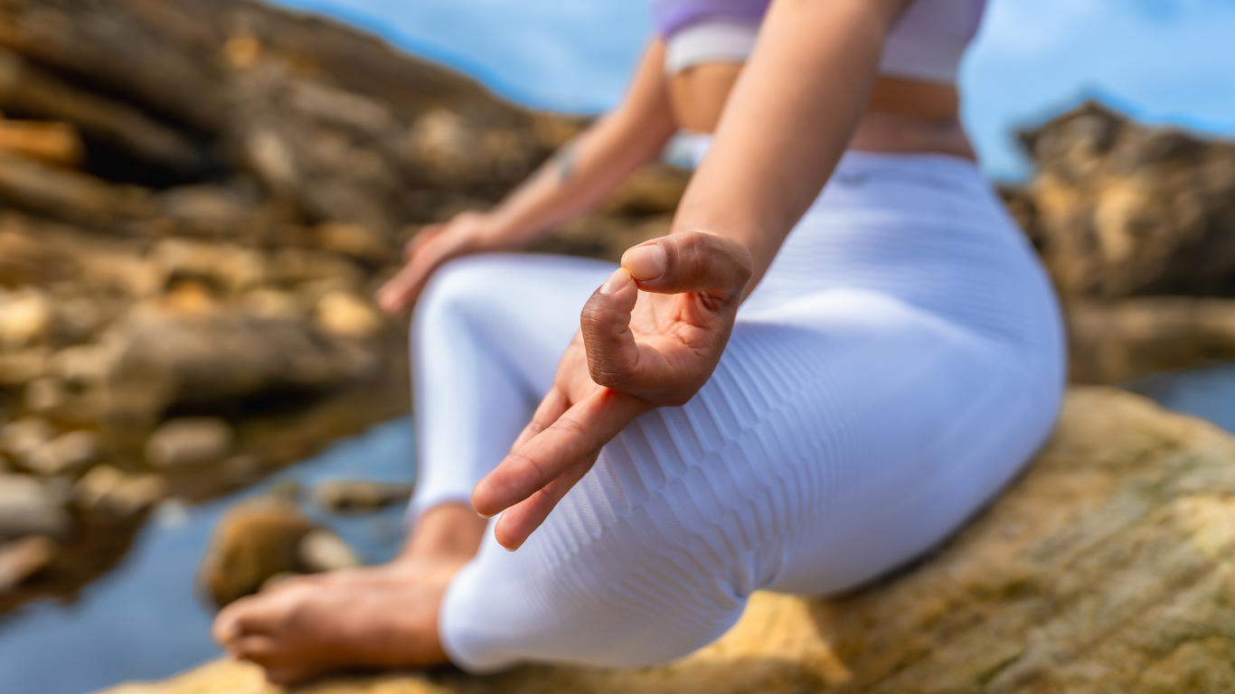 Silhouette of a person meditating on grass at sunset with a bright sky behind.