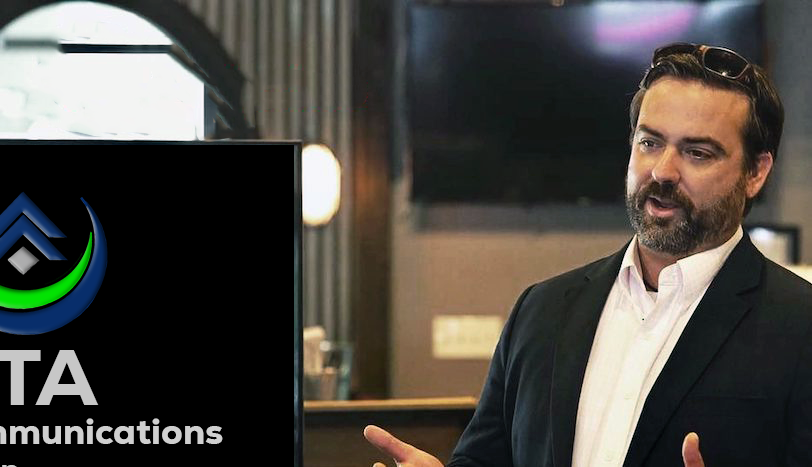 A man in a suit is standing in front of a sign that says communications