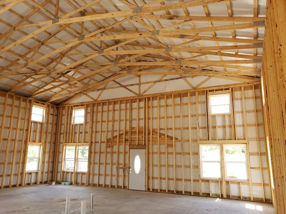 Interior view of a building under construction, featuring wooden framing, arched roof beams, windows, and a doorway.