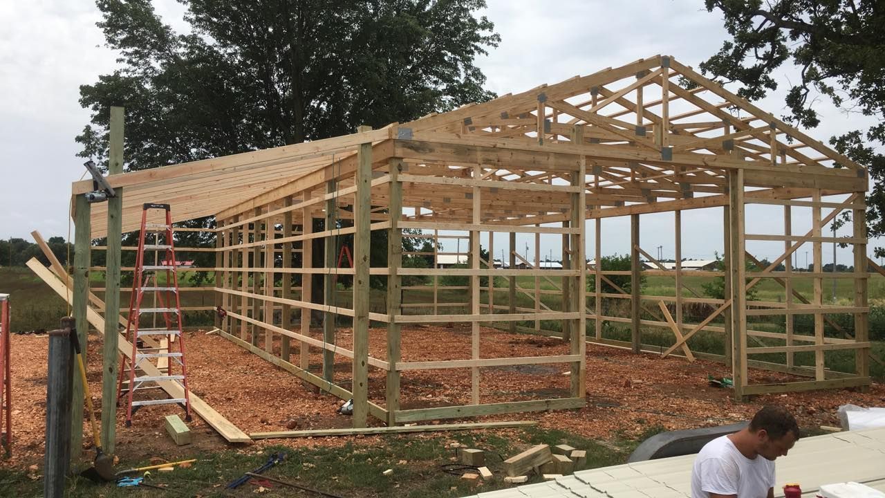 Wooden barn under construction on a gravel bed; person in white shirt visible.