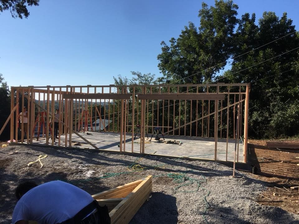 Wooden framework of a building under construction on a gravel surface, with trees in the background.