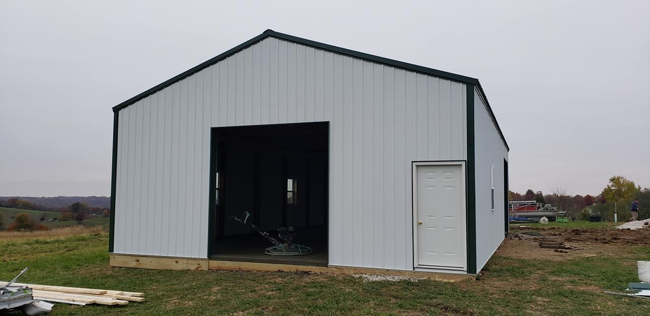A white metal building with a green trim and an open doorway and a side door on a grassy field.