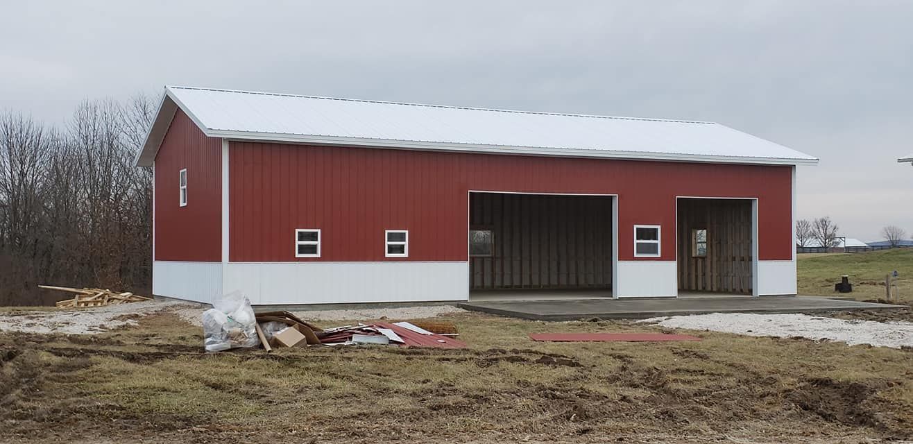 Red barn with white trim and a snow-covered roof. It has two garage door openings and small windows. Cloudy sky.